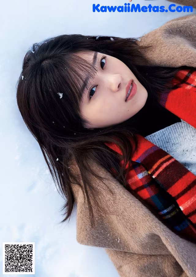 A woman laying in the snow wearing a coat and scarf.
