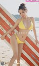 A woman in a yellow bikini holding a surfboard on the beach.