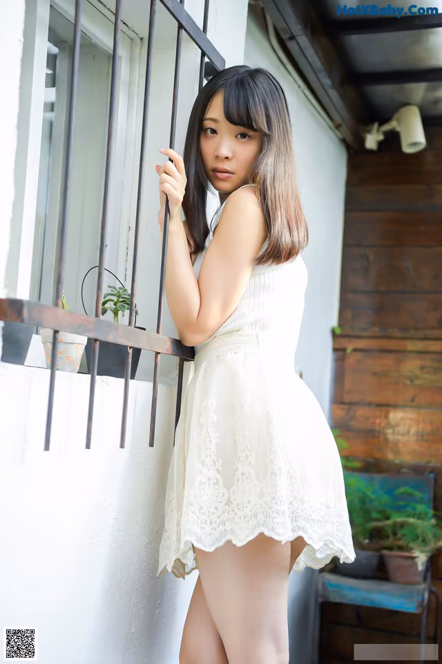 A woman in a white dress leaning against a window.