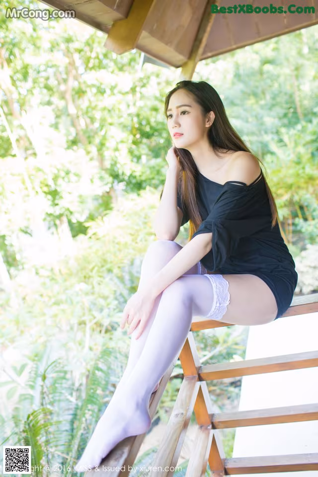 A woman sitting on a wooden bench in a black top and white stockings.