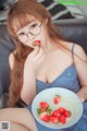 A woman sitting on a couch eating a bowl of strawberries.