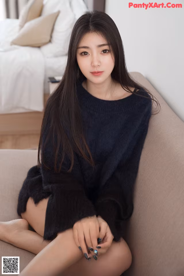 A woman sitting on a couch wearing a black sweater.
