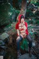 A woman in a red hooded outfit sitting on a rock in the woods.