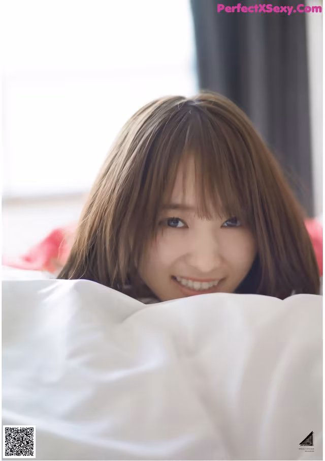 A young woman laying in bed smiling at the camera.