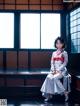 A woman in a kimono sitting on a bench in front of a window.