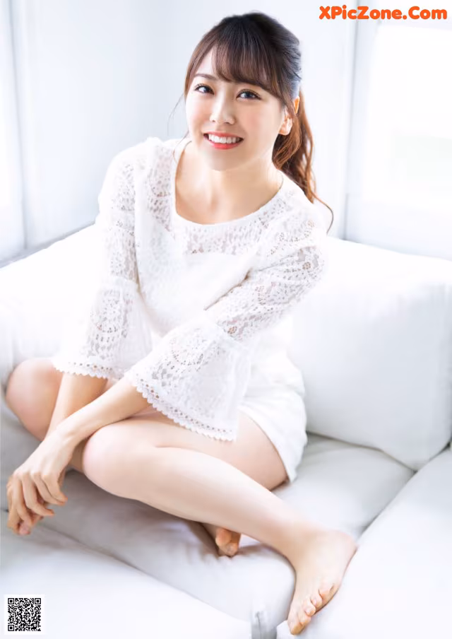 A woman sitting on a white couch with her legs crossed.