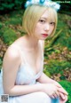 A woman in a white dress sitting on a moss covered ground.