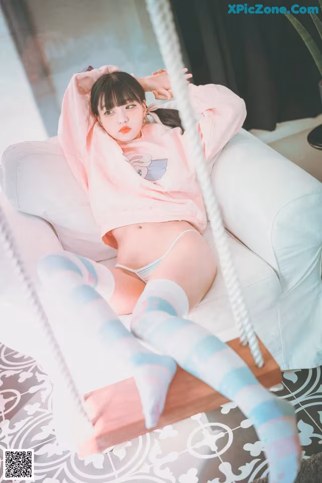 A woman sitting on a white chair wearing a pink sweatshirt and blue socks.