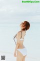 A woman in a white bikini standing on the beach.