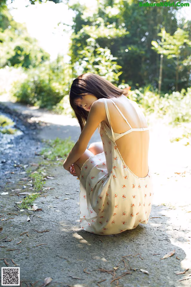 A woman in a white dress sitting on a dirt road.