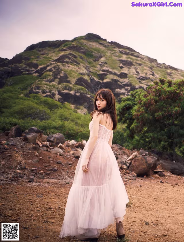 A woman in a white dress standing on a dirt road.