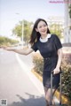 A woman in a black dress with a suitcase on the street.