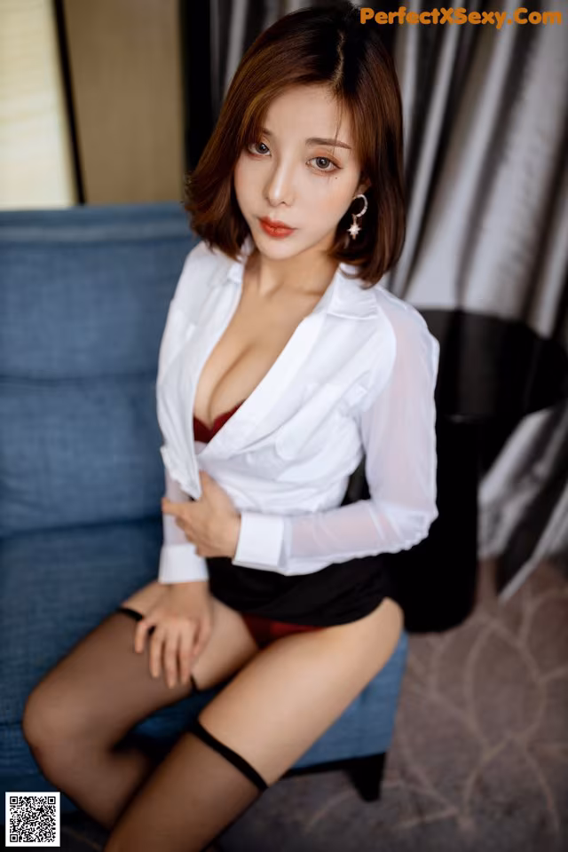 A woman in a white shirt and black skirt sitting on a blue couch.