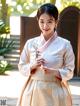 A woman in a white and pink hanbok holding a flower.