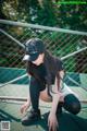 A woman crouching down on a tennis court wearing a baseball cap.