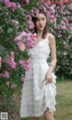 A woman in a white dress standing in front of pink flowers.