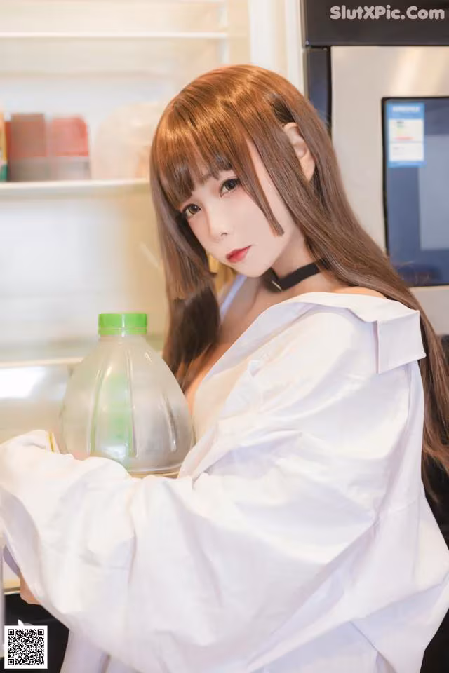 A woman holding a bottle of water in front of a refrigerator.