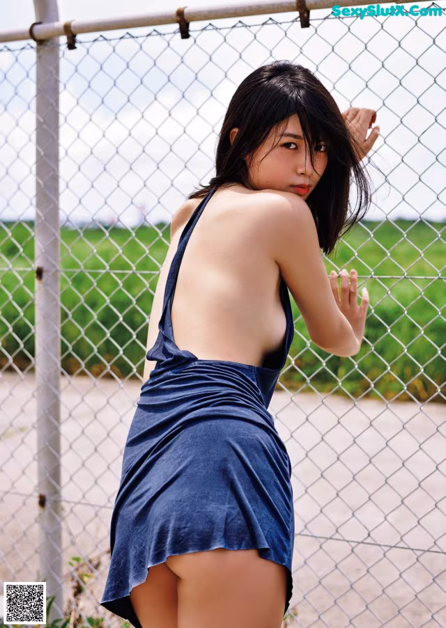 A woman in a blue dress leaning against a fence.