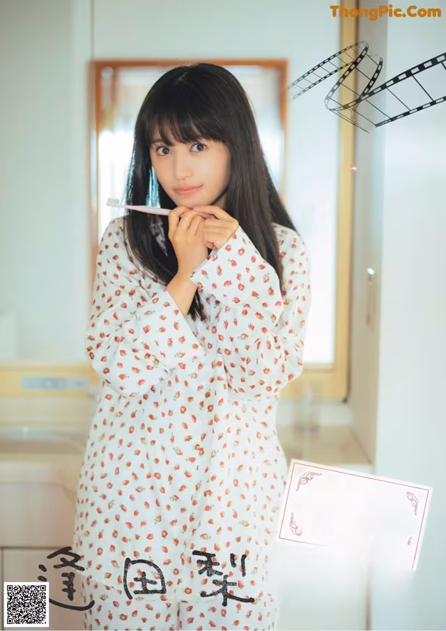 A woman in pajamas brushing her teeth in front of a mirror.